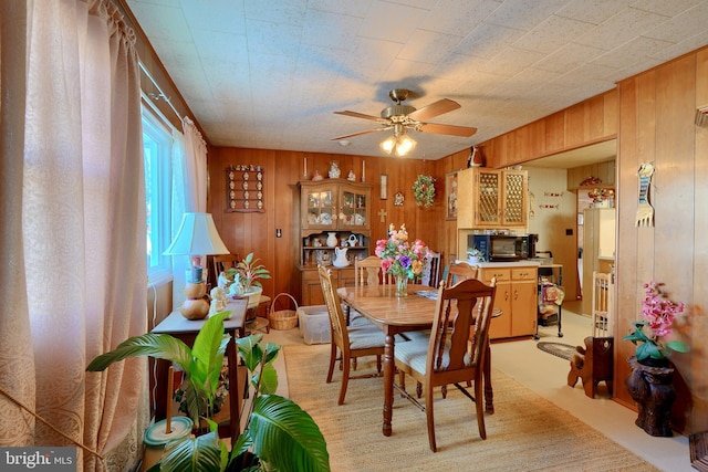 carpeted dining space featuring ceiling fan and wood walls