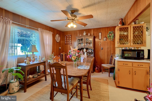 dining room featuring ceiling fan, light carpet, and wooden walls