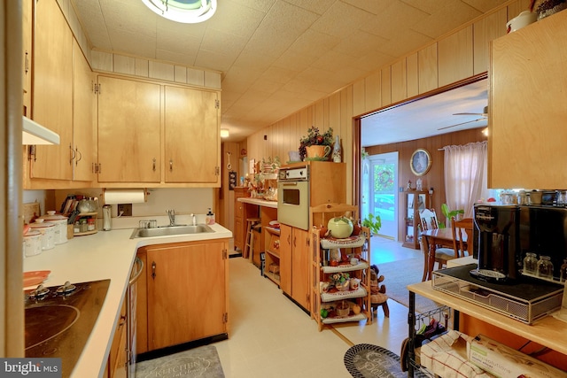 kitchen featuring wood walls, oven, sink, ceiling fan, and stovetop