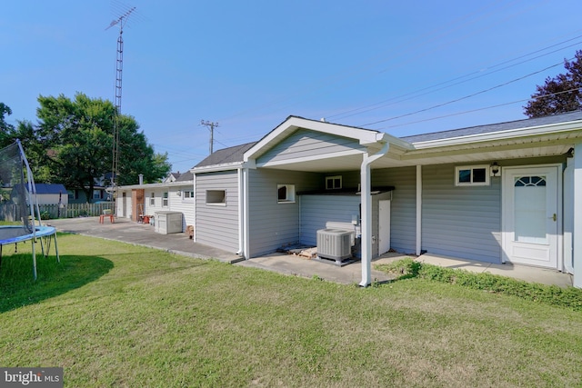 rear view of property featuring central AC, a yard, a patio, and a trampoline