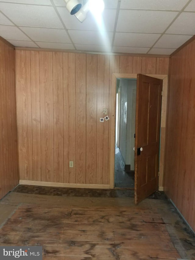 unfurnished room featuring wood walls, dark hardwood / wood-style flooring, and a drop ceiling