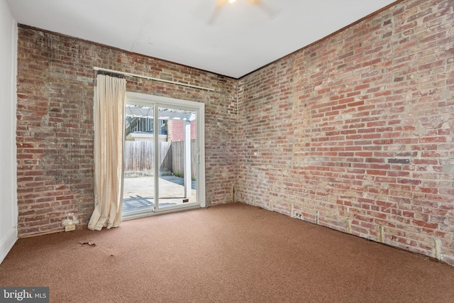 carpeted spare room featuring ceiling fan and brick wall