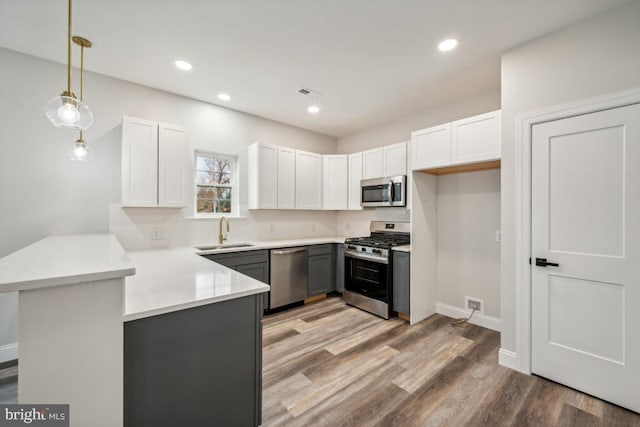 kitchen featuring kitchen peninsula, appliances with stainless steel finishes, decorative light fixtures, white cabinets, and sink