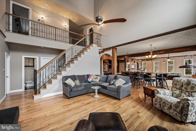 living room with ceiling fan with notable chandelier, a towering ceiling, light wood-type flooring, and beamed ceiling