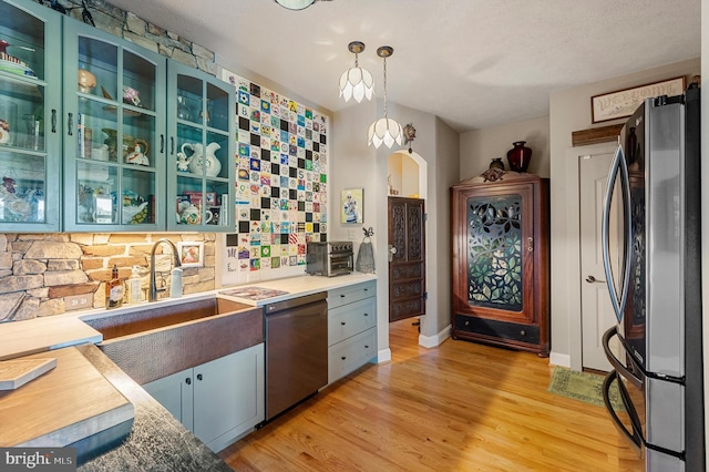 kitchen featuring sink, decorative light fixtures, a textured ceiling, light wood-type flooring, and appliances with stainless steel finishes