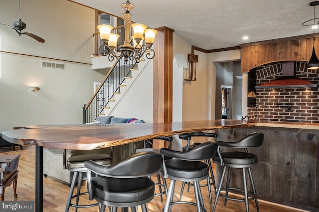 bar featuring ceiling fan with notable chandelier, a textured ceiling, crown molding, and wood-type flooring