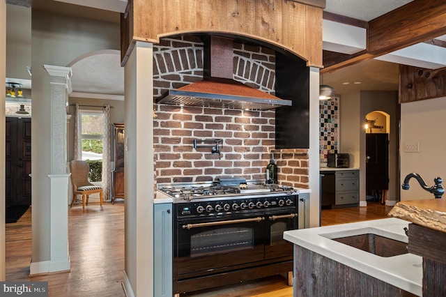 kitchen with ornate columns, light wood-type flooring, double oven range, wall chimney exhaust hood, and sink