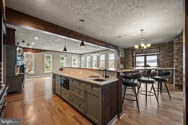 kitchen with light hardwood / wood-style floors, beam ceiling, a large island with sink, black microwave, and sink