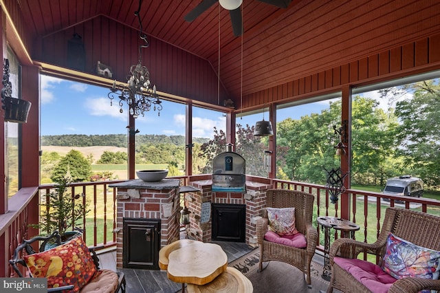 sunroom / solarium featuring a wealth of natural light, ceiling fan with notable chandelier, an outdoor brick fireplace, and lofted ceiling