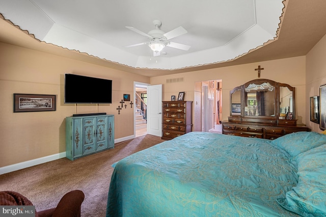 carpeted bedroom with a raised ceiling and ceiling fan