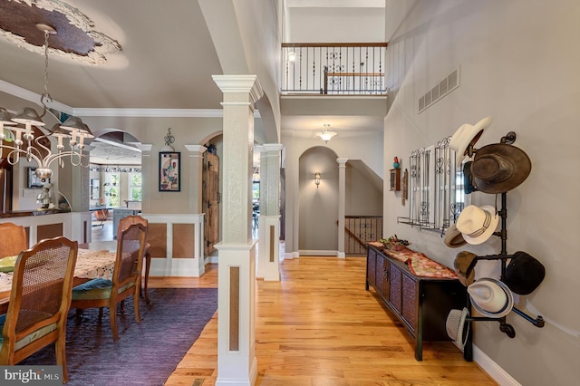 entryway featuring light hardwood / wood-style floors, a notable chandelier, ornamental molding, and ornate columns