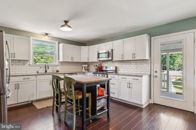 kitchen with white cabinetry, decorative backsplash, dark wood finished floors, a sink, and appliances with stainless steel finishes