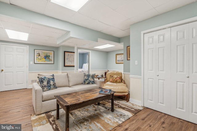 living area featuring visible vents, a drop ceiling, light wood-type flooring, and wainscoting