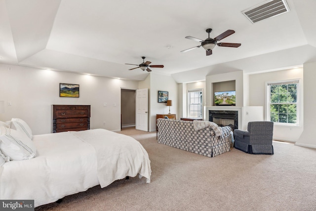 bedroom featuring vaulted ceiling, a ceiling fan, a fireplace, light colored carpet, and visible vents