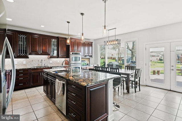 kitchen featuring dark stone counters, an island with sink, sink, appliances with stainless steel finishes, and light tile patterned floors