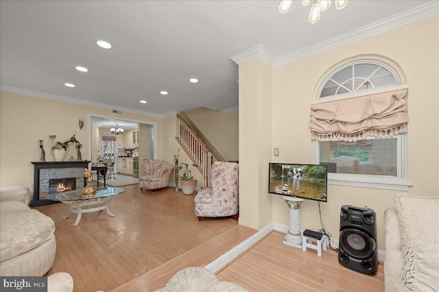 living room with a fireplace, a notable chandelier, ornamental molding, and hardwood / wood-style flooring