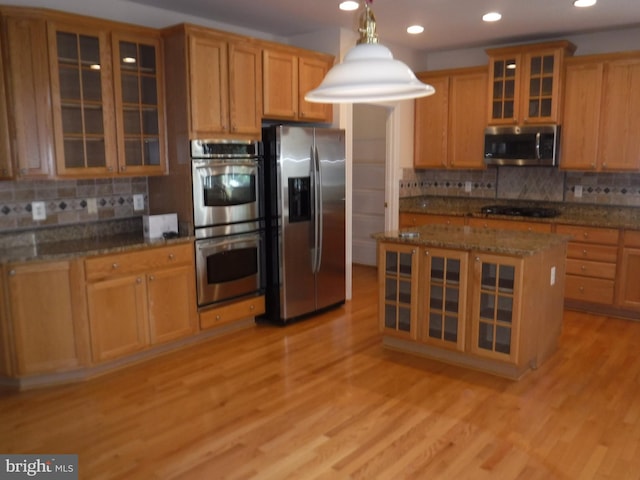 kitchen featuring stainless steel appliances, light hardwood / wood-style flooring, hanging light fixtures, and dark stone countertops