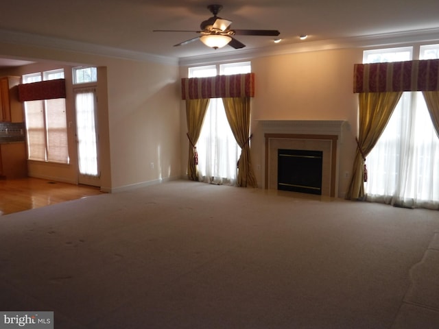 unfurnished living room with ceiling fan, a healthy amount of sunlight, crown molding, and light carpet