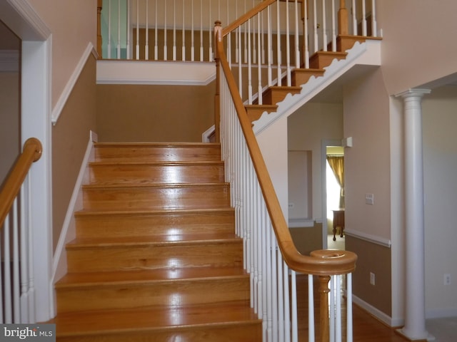 stairway featuring a towering ceiling, hardwood / wood-style flooring, and ornate columns