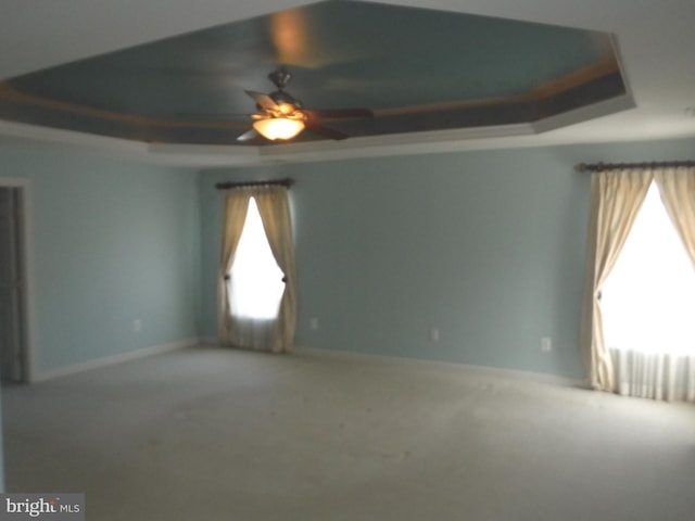 carpeted spare room featuring a raised ceiling and ceiling fan