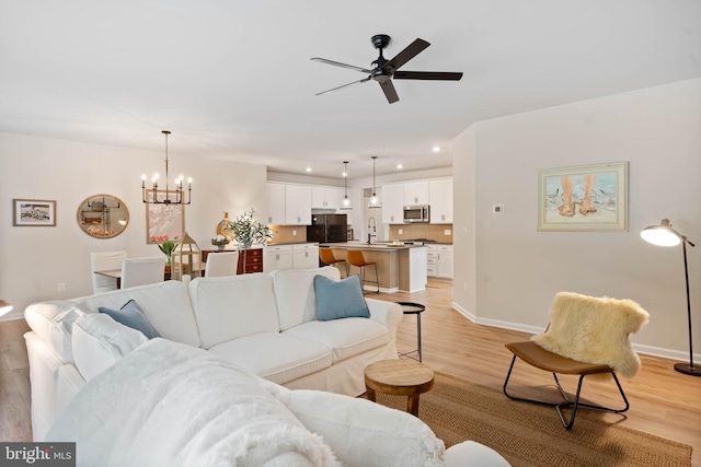 living room featuring light hardwood / wood-style flooring, sink, and ceiling fan with notable chandelier