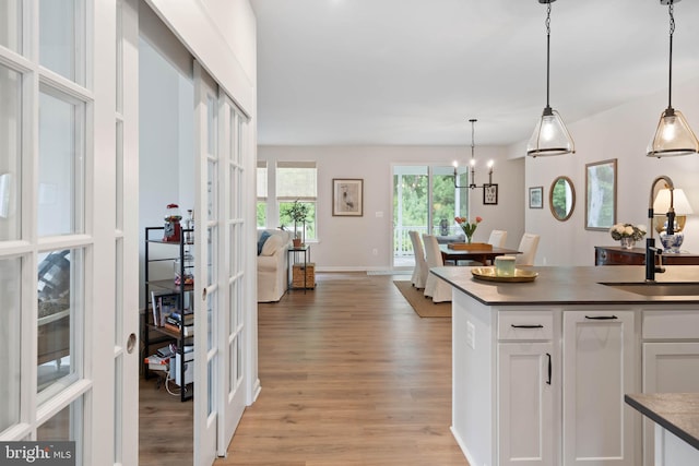 kitchen with light hardwood / wood-style flooring, white cabinets, pendant lighting, an inviting chandelier, and sink