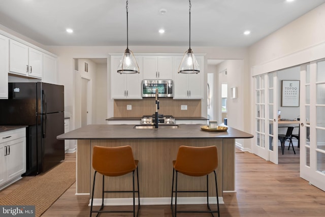 kitchen with backsplash, a kitchen island with sink, white cabinetry, and light hardwood / wood-style floors