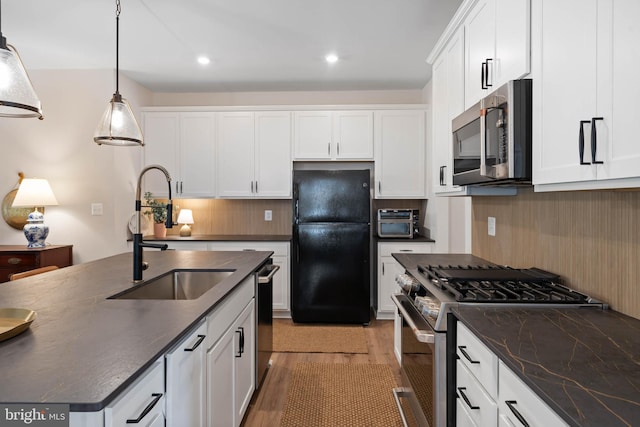 kitchen with decorative backsplash, appliances with stainless steel finishes, a kitchen island with sink, light hardwood / wood-style flooring, and decorative light fixtures