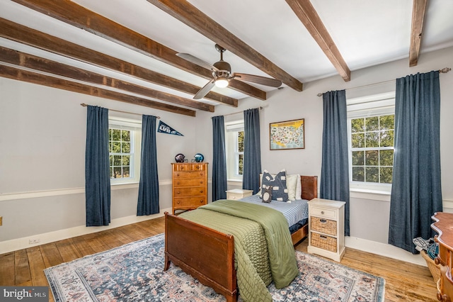 bedroom featuring ceiling fan, multiple windows, hardwood / wood-style floors, and beamed ceiling