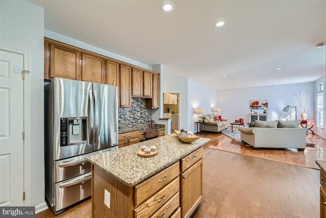 kitchen featuring stainless steel fridge, tasteful backsplash, light stone counters, a center island, and light hardwood / wood-style floors