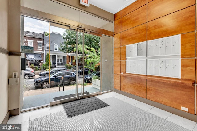 doorway to outside with mail boxes, wooden walls, and light tile patterned floors