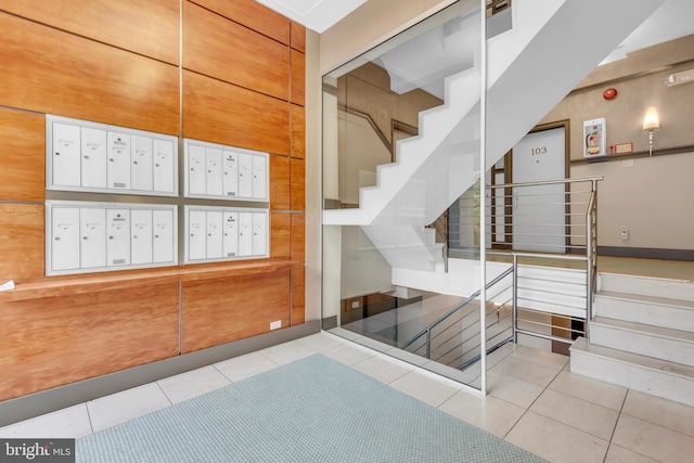 stairway with wooden walls, tile patterned flooring, a towering ceiling, and a mail area