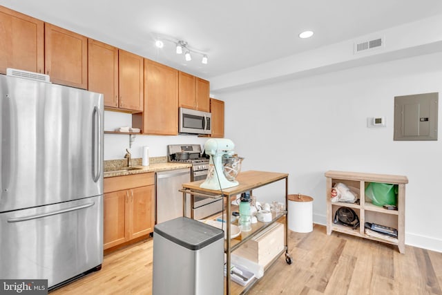 kitchen with electric panel, sink, light wood-type flooring, appliances with stainless steel finishes, and light stone counters