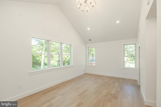 spare room featuring high vaulted ceiling, light wood-type flooring, and an inviting chandelier