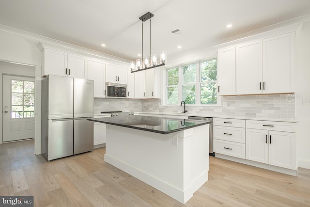 kitchen featuring stainless steel appliances, decorative light fixtures, light wood-type flooring, a kitchen island, and white cabinets