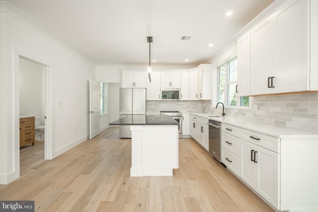 kitchen featuring white cabinets, a kitchen island, stainless steel appliances, sink, and hanging light fixtures