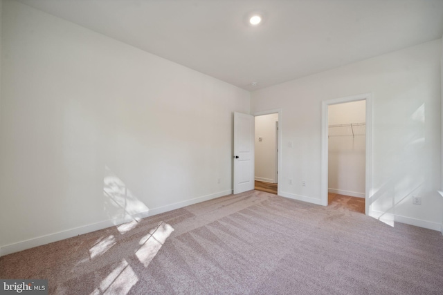 unfurnished bedroom featuring a walk in closet, light colored carpet, and a closet