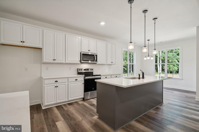 kitchen with white cabinets, appliances with stainless steel finishes, decorative light fixtures, and an island with sink