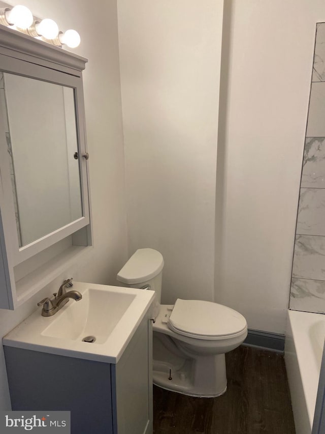 bathroom featuring toilet, a tub, hardwood / wood-style flooring, and vanity