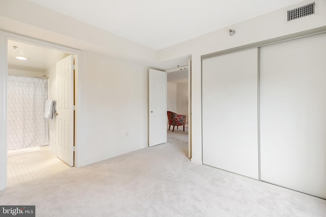 unfurnished bedroom with visible vents, ensuite bathroom, a closet, and light colored carpet