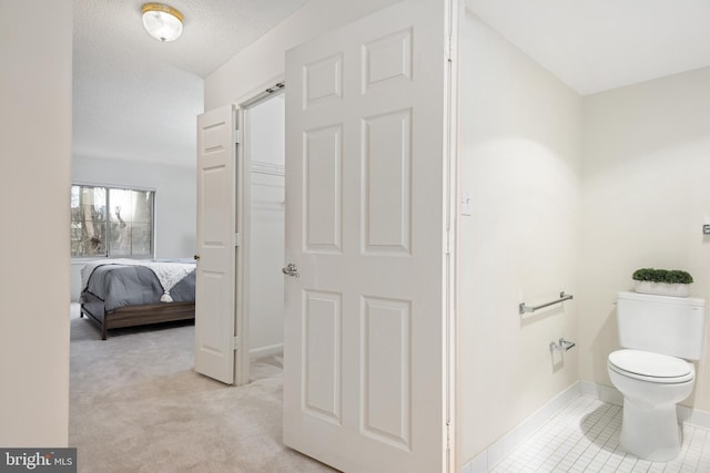 bathroom with a textured ceiling, tile patterned floors, toilet, and baseboards