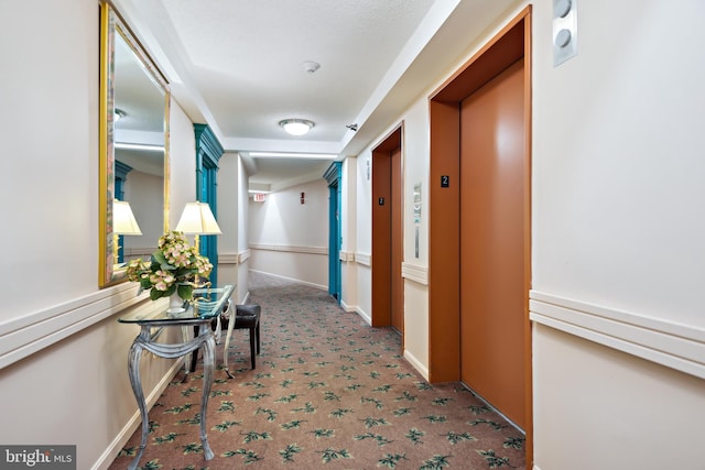 corridor featuring elevator, baseboards, and carpet flooring