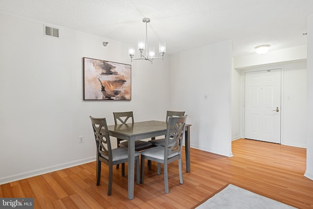 dining room featuring baseboards, visible vents, wood finished floors, a textured ceiling, and a notable chandelier