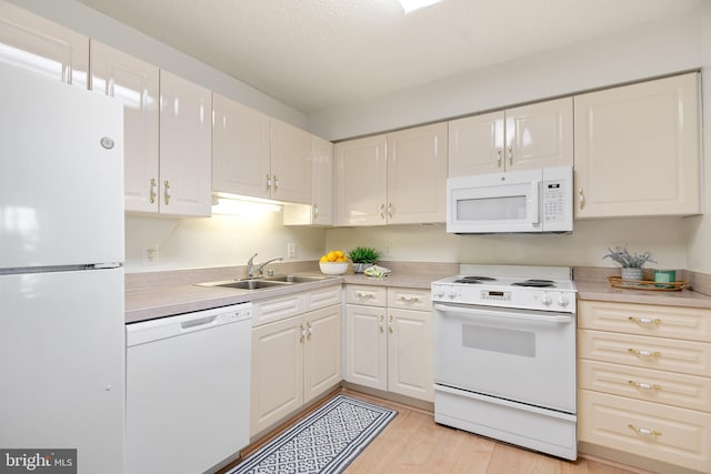 kitchen with white appliances, light countertops, light wood-type flooring, white cabinetry, and a sink