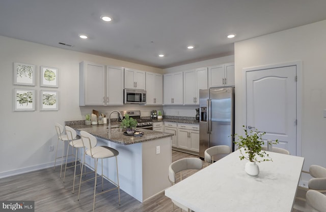 kitchen featuring hardwood / wood-style floors, a kitchen bar, dark stone countertops, kitchen peninsula, and stainless steel appliances