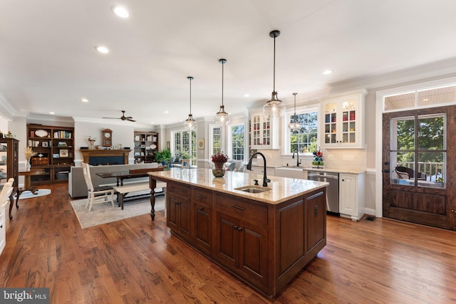 kitchen featuring sink, light stone counters, a center island with sink, stainless steel dishwasher, and pendant lighting