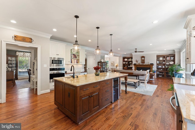 kitchen with white cabinetry, hanging light fixtures, light stone counters, stainless steel appliances, and a center island with sink