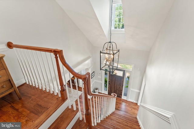 stairs featuring hardwood / wood-style flooring, lofted ceiling, and a notable chandelier