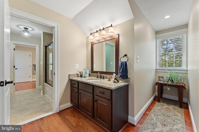 bathroom with vanity, wood-type flooring, bath / shower combo with glass door, and vaulted ceiling