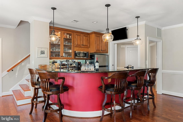 bar featuring pendant lighting, appliances with stainless steel finishes, dark wood-type flooring, and dark stone countertops